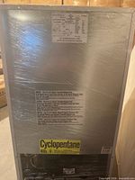 Rear view of shrink-wrapped Insignia mini fridge showing model label and compressor area