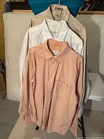 Three shirts hanging: peach, white, beige
