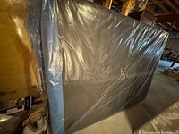 Full view of gray queen box spring wrapped in clear plastic