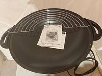 Electric wok interior with wire rack and manuals visible
