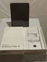 Tablet standing upright behind open box displaying accessories