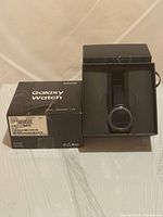 Galaxy Watch on charging tray inside open retail box alongside outer box showing label and Galaxy Watch branding