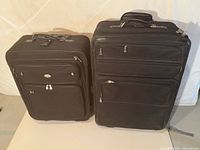 Front view of both black suitcases showing size difference, exterior zip pockets, wheels and handles