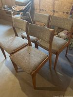 Four chairs angled, showing teak frames and worn beige fabric seats