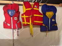 Three Buoy-O-Boy youth life jackets hanging, showing colours and front fastenings