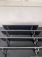 Four black shelves stacked showing brackets and finish