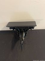 Top view of black Gothic wall shelf bracket showing bird skull motif and shelf surface