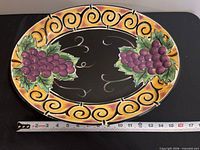 Top view of Clay Art ceramic platter showing grape motif and scroll border with ruler for scale