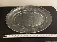 Top view of clear glass oval platter showing embossed leaf and berry design with ruler for scale