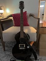 Front view of black Epiphone Les Paul style guitar on chair