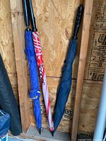 Three folded golf umbrellas leaned against wall showing canopy colors and handles