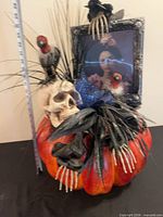 Front view showing pumpkin base, skull, birds, skeleton hands, frame and floral accents