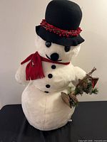 Front view of plush snowman with hat, scarf, buttons and attached birdhouse garland