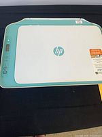 Closed printer showing teal/aqua and white exterior with HP logo