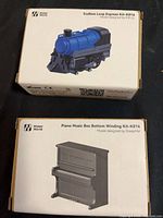 Two Maker World kit boxes showing locomotive and piano models