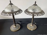 Pair of bronze-tone metal table lamps with frosted etched glass shades on black surface