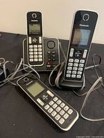 Three Panasonic handsets, main base with keypad, single satellite cradle, cables visible