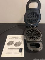 Open waffle maker with manual and latch adapter visible