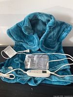 Front view of teal wearable heating pad with controller and AC cord visible