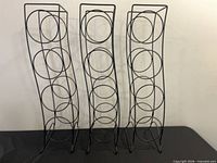 Front view of three identical black metal wine racks showing five circular holders each