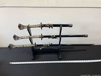 Full view of three swords in scabbards on display stand with ruler for scale