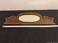 Front view showing full carved wood frame and oval mirror with measuring tape for length reference