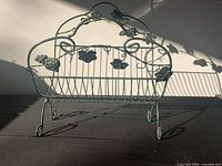 Front view of green metal magazine rack showing grapevine scrollwork and slatted basket