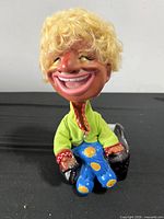 Front view of seated laughing bobble head man showing face, clothing, and chair base