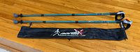 Two blue Nordixx telescopic walking poles and branded black carry bag on wooden floor