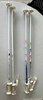 Both pairs of white ski poles standing upright showing full length and grips