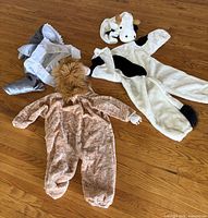Three children’s costumes laid out on wood floor: gray shark, tan lion, white cow