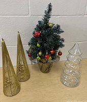 Group shot of all items: two gold wire cone trees, artificial green tree with ornaments, glass candy jar
