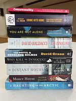 Stack of nine paperback books showing front edges and titles