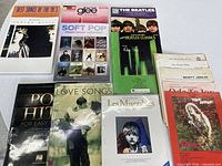 Overview of all nine piano songbooks and stack of loose sheet music
