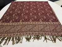 Shawl laid flat showing burgundy side with paisley border and fringe