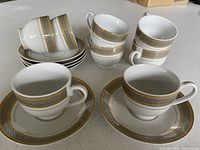 Group of eight teacups and six saucers showing Greek key pattern and gold trim