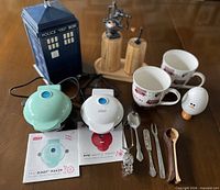 Group shot of Dash appliances, TARDIS tin, mugs, grinders, utensils, manuals