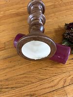 Underside and side view of brown pottery candlestick with Lenox mark beside burgundy candle, partial wreath visible