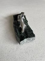 Angled view of entire sculpture showing two polished metal seals on dark green stone base