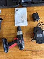 Jobmate 18V cordless drill, manual, charger base, AC adapter and part of carrying case on wooden floor