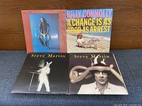 Front covers of four comedy LPs lined up on a sofa: George Carlin, Billy Connolly, two Steve Martin