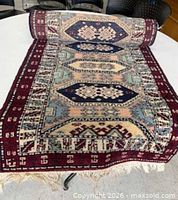 Top view of rolled synthetic geometric medallion runner rug showing colors, pattern and fringe