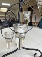 Close view of black metal scroll frame with attached clear glass cup