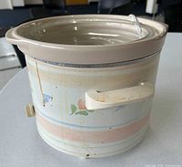 Side view showing handles, rim, interior ceramic insert and glass lid