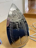 Front view of stainless steel soleplate with vent holes and visible staining, power cord visible