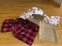 All items grouped: two red/black plaid tablecloths, white heart-pattern tablecloth, four bamboo placemats, woven basket