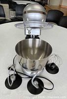 Front view of stand mixer with bowl, splash guard, whisk and dough hooks displayed