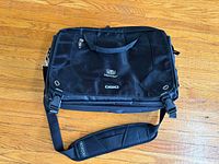 Front view of black OGIO TripAdvisor carry-on bag with shoulder strap attached