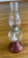 full view of glass oil lamp showing red base, clear font, brass burner and chimney