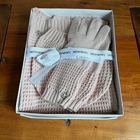 Open box showing pink knit scarf, hat and gloves with Calvin Klein ribbon and tags